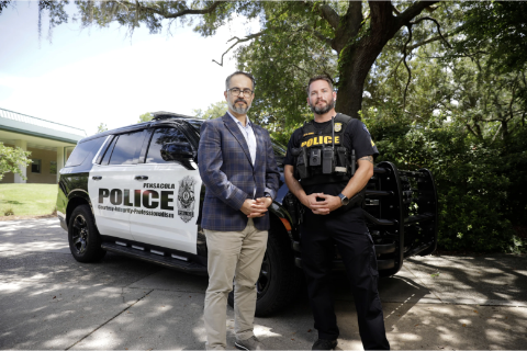 UWF faculty Nicholas Buker standing in front of a police vehicle with a local police officer. with local